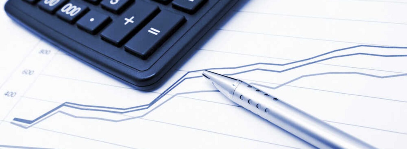 Na stole leży kalkulator i długopis, pod nimi widać wykresy.
