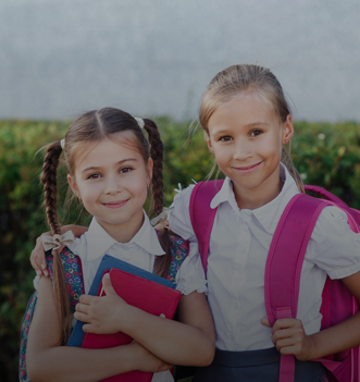 Dwie uczennice w mundurkach szkolnych stoją obok siebie z książkami i plecakami