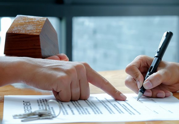 Najem okazjonalny mieszkania Dwie osoby podpisują umowę najmu okazjonalnego mieszkania, obok znajduje się miniaturowy model domu