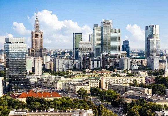 Widok na nowoczesne centrum Warszawy w słoneczny dzień, z charakterystycznym Pałacem Kultury i Nauki oraz otaczającymi go wysokimi budynkami biurowymi. Tło idealne do tematu podróży i korzystania z karty EKUZ podczas zagranicznych wizyt.