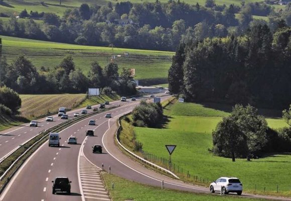 Pojazdy poruszające się po wielopasmowej drodze wśród zielonych wzgórz, zdjęcie pokazuje ruchliwy szlak komunikacyjny.