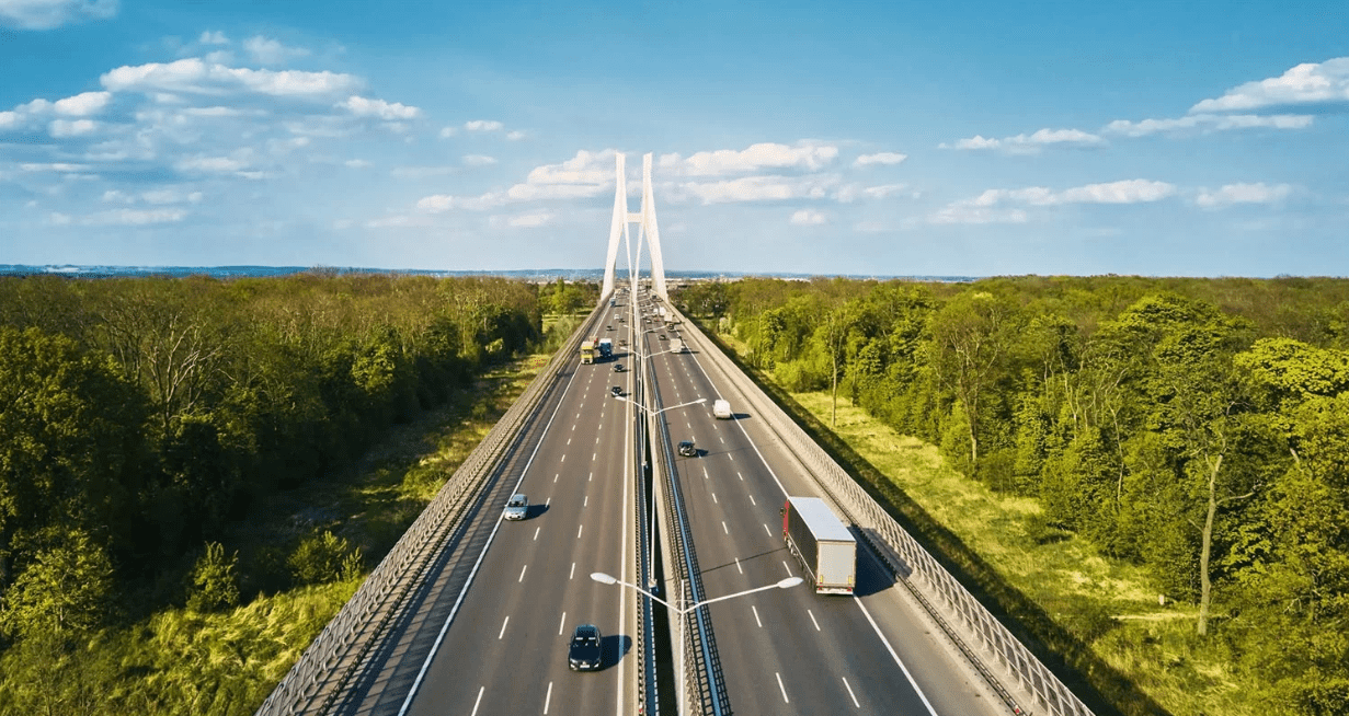 Widok na nowoczesny wielopasmowy autostradowy most z białymi kablami, po którym poruszają się różne pojazdy w obu kierunkach, z ciężarówką i samochodami osobowymi – potencjalny przykład drogi objętej systemem opłat drogowych eurowinieta