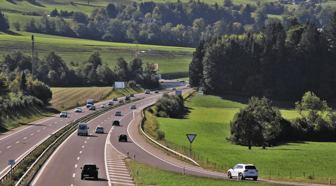 Pojazdy poruszające się po wielopasmowej drodze wśród zielonych wzgórz, zdjęcie pokazuje ruchliwy szlak komunikacyjny.