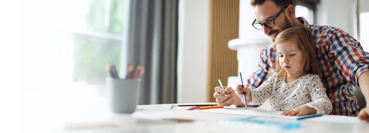 Osoba dorosła i dziecko siedzą przy stole, rysując kolorowymi kredkami na białych kartkach